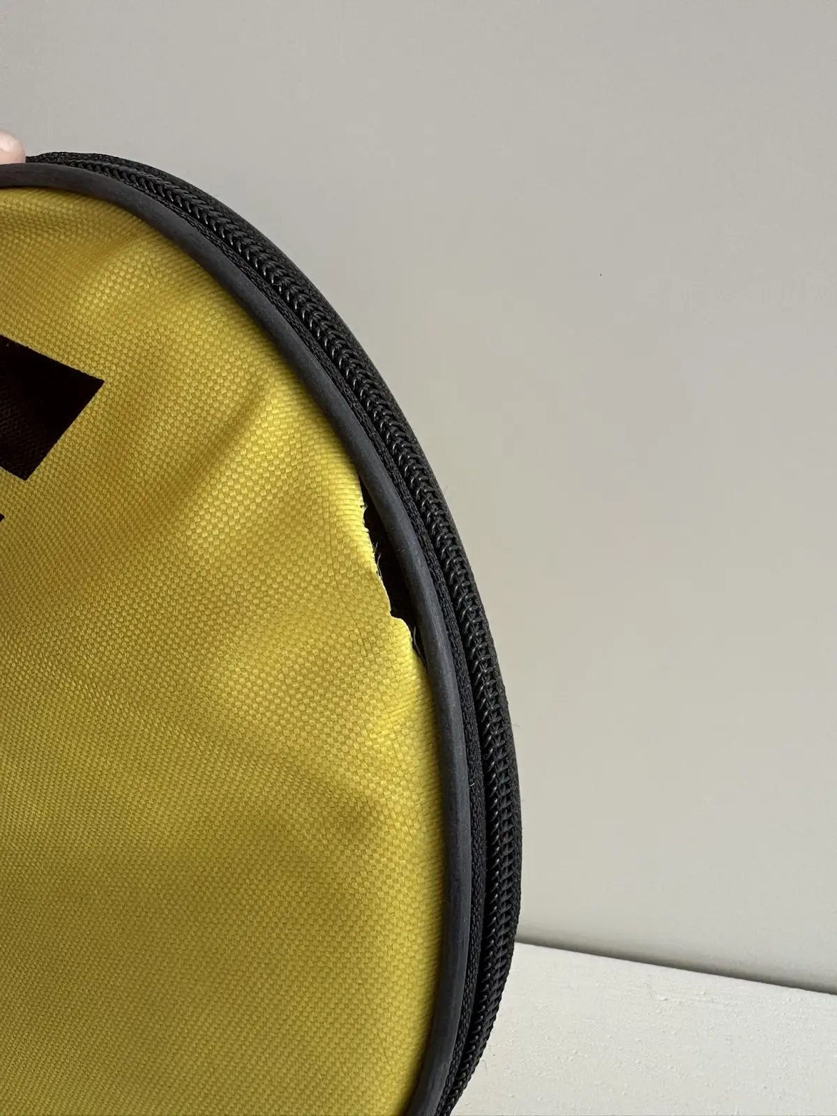 Close-up of a round yellow textured fabric case with a black zipper and a small tear along the inner edge, photographed against a light gray background.